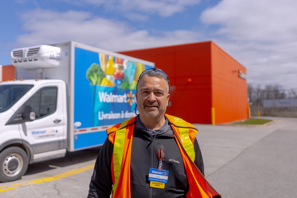 Walmart associate John stands in front of a Walmart truck, smiling at the camera. 