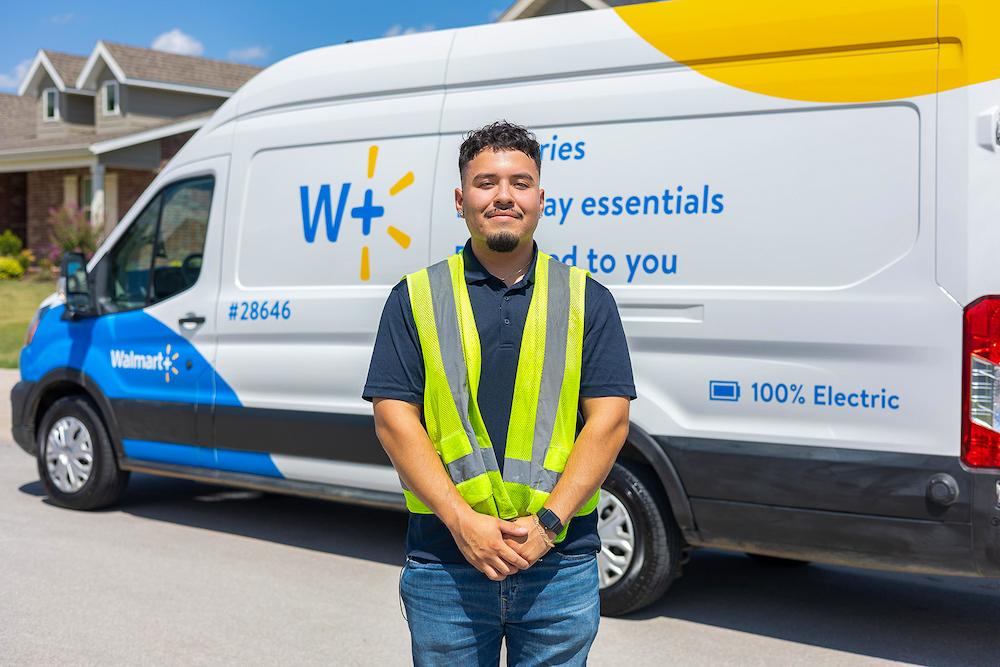 A Walmart associate wears a bright vest in front of an electric Walmart van.