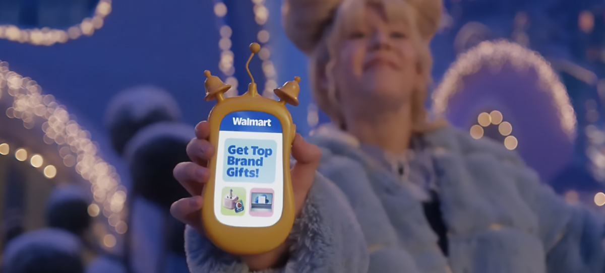 A yellow handheld device displays a Walmart message reading 'Get Top Brand Gifts!' against a festive background. The setting features glowing holiday lights and snow-covered visuals, evoking a cheerful winter atmosphere.