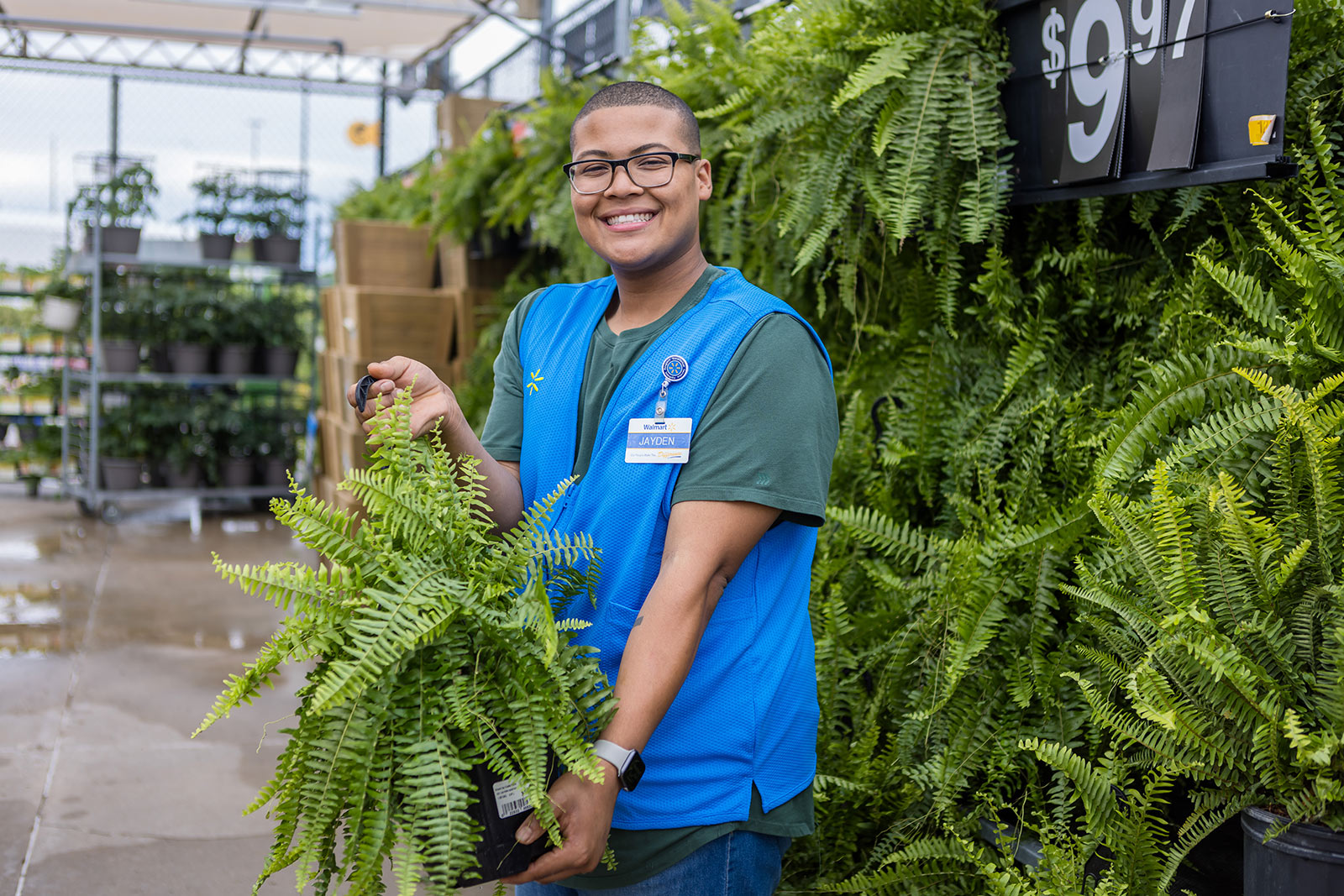 A Walmart associate working in garden section holding a hanging basket of fern.