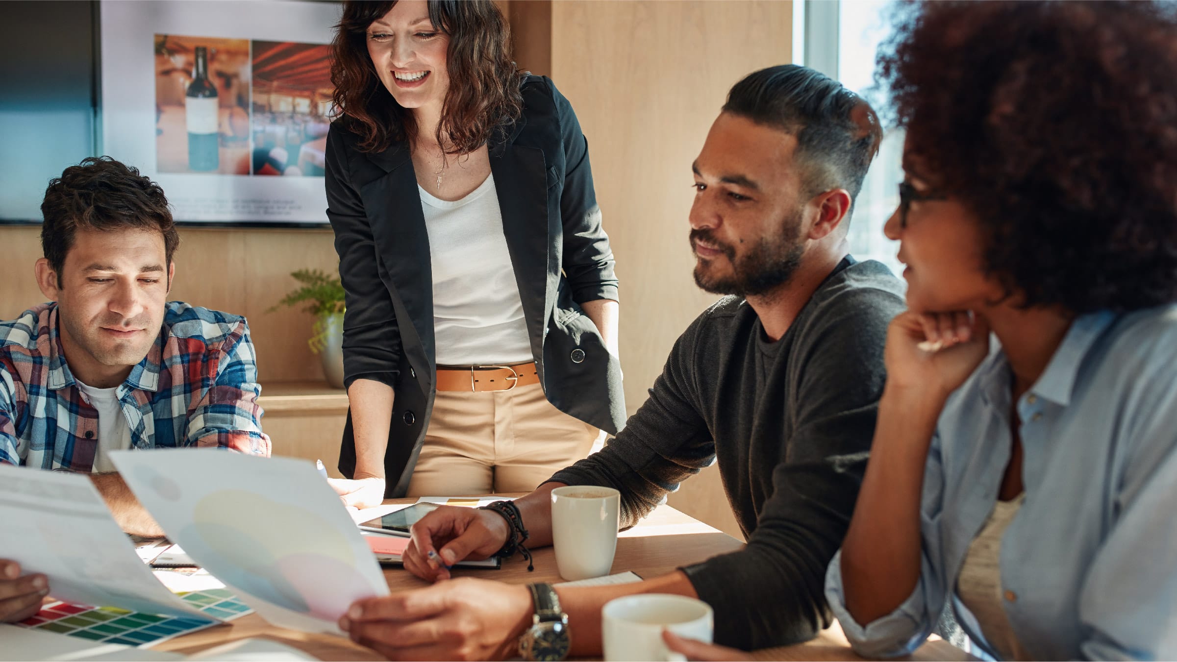 A group of four coworkers gather around a desk looking together at pages of charts.